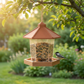 Gazebo hanging bird feeder with a terracotta roof hanging from a tree branch, a chickadee feeding at the tray